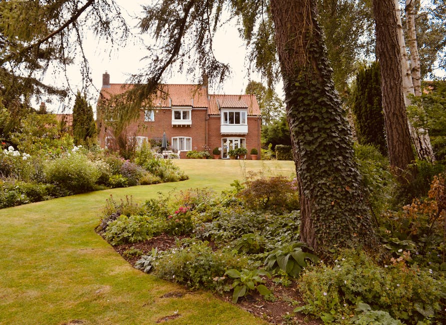 A front garden area in front of a traditional red brick house featuring a white wooden front door with a small window panel, arched door frame, and house number plaque. The garden includes neatly trim